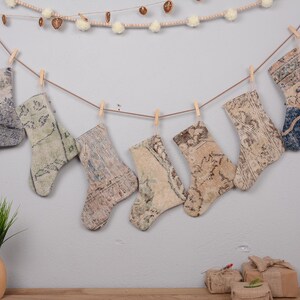 May include: A set of seven decorative Christmas stockings made from repurposed rugs. The stockings are hung on a string with clothespins and feature a variety of patterns and colors, including blue, green, and beige.