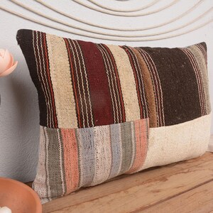 Könnte beinhalten: Rechteckiges Kissen mit Patchwork-Design. Der obere Bereich hat vertikale Streifen in Braun, Beige und Burgunder. Der untere Bereich hat Streifen in Grau, Pfirsich und Beige. Das Kissen liegt auf einer Holzoberfläche.