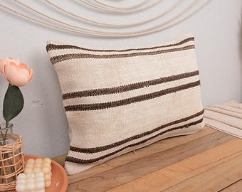 May include: A white and brown striped throw pillow with a linen texture. The pillow is on a wooden surface.