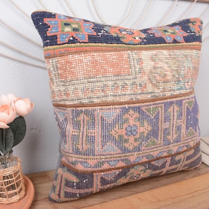 May include: A decorative pillow with a patchwork design. The pillow features sections of patterned fabric in shades of blue, peach, and beige. The pillow is square and appears to be made of a woven material. The pillow is on a wooden surface.