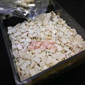 Op de afbeelding: Een grote hoeveelheid kleine, gebroken witte plastic eindkappen in een doorzichtige plastic container.