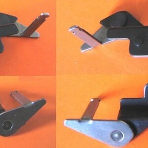 May include: Four black metal brackets with silver-colored levers and circular holes. The brackets are arranged in a grid pattern against an orange background. Each bracket has a unique shape and design.