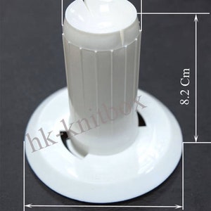 Op de afbeelding: Witte plastic garen houder met een bovenste opening van 3,8 cm diameter, een hoogte van 8,2 cm en een basis van 9,5 cm diameter.