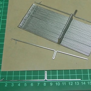 Può includere: Un set di ferri da maglia argentati con uno strumento a forma di T per unire i ferri. I ferri sono disposti in una pila e lo strumento è su un tappetino da taglio verde.