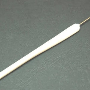 Puede incluir: Un ganchillo blanco con un mango largo y cilíndrico y un gancho de metal en el extremo. El ganchillo está diseñado para manualidades y es adecuado para varios grosores de hilo y proyectos. La herramienta se muestra sobre un fondo oscuro.