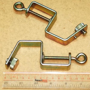May include: Two gold metal clamps with a screw adjustment and a hook on one end. The clamps are approximately 5 cm in length.
