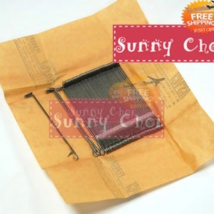 May include: A pack of 100 silver sewing machine needles, packaged in a brown paper envelope. The needles are arranged in a neat stack and are ready to be used for sewing projects.