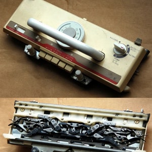 May include: A white and beige knitting machine with a handle and a dial. The machine has a series of buttons and a red stripe. The bottom of the machine is open, revealing a series of metal hooks and gears.