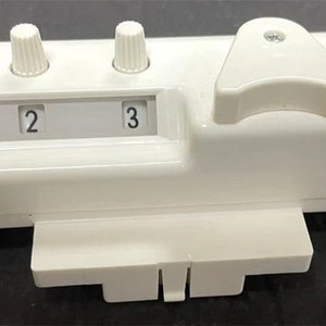 Könnte beinhalten: Weißes Plastikgerät mit drei Knöpfen und einem Hebel. Die Knöpfe sind mit 1, 2 und 3 beschriftet.