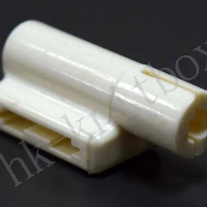 May include: A white plastic connector with a slot and a round opening. The connector is designed for electrical wiring.