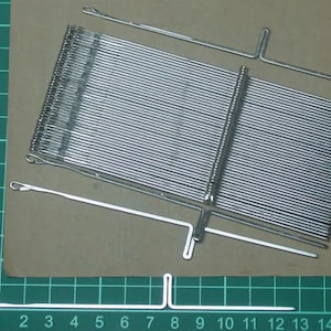 May include: A set of silver knitting needles with a hook on one end and a T-shaped end on the other. The needles are arranged in a grid pattern and are approximately 15 cm long.