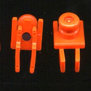 Puede incluir: Cuatro piezas de juguete de plástico naranja con diferentes diseños. Dos piezas tienen una parte superior redonda con dos puntas en la parte inferior. Las otras dos piezas tienen una parte superior plana con dos puntas en la parte inferior.