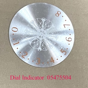 Puede incluir: Un indicador de dial plateado con un diseño de copo de nieve y números del 0 al 8 alrededor del borde. El texto "Dial Indicator 05475504" está impreso debajo del dial.