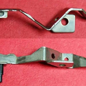 May include: Two metal sewing machine parts. The first part is a silver, curved metal piece with a hole in the center. The second part is a silver, straight metal piece with a small, silver pin extending from the side.