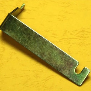 May include: A metal tool with a bent handle and a hook on one end. The tool is silver in color and has a shiny finish.