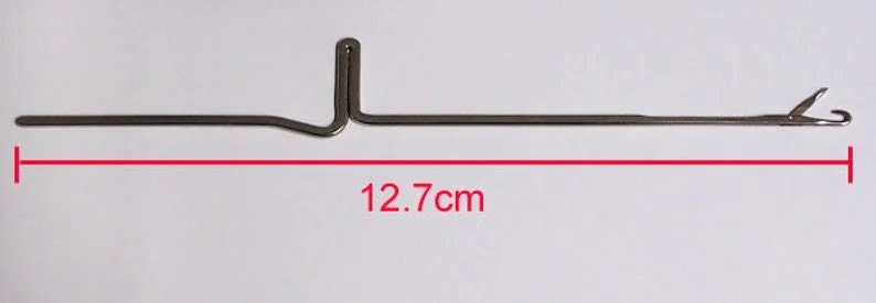 K&ouml;nnte beinhalten: Eine silberne Stricknadel mit einem Haken an einem Ende und einer Schlaufe am anderen. Die Nadel ist 12,7 cm lang.