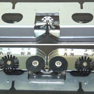 May include: A close-up of a silver metal mechanism with two black gears and a silver metal hinge. The mechanism is designed to move back and forth.