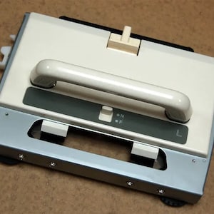 May include: A white and gray knitting machine with a handle and a switch labeled "N" and "F".