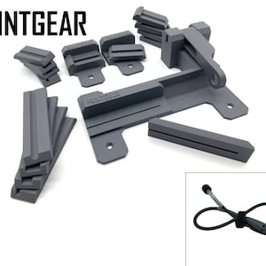 Könnte beinhalten: Ein graues 3D-gedrucktes Werkzeug zum Halten und Sichern eines kleinen Objekts. Das Werkzeug verfügt über eine Klemme, einen Hebel und eine Basis. Das Werkzeug ist mit "PRINTGEAR" beschriftet.