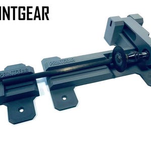 Peut inclure: Un outil gris imprimé en 3D pour maintenir et faire tourner un petit outil électrique. L'outil porte l'inscription "PRINTGEAR".