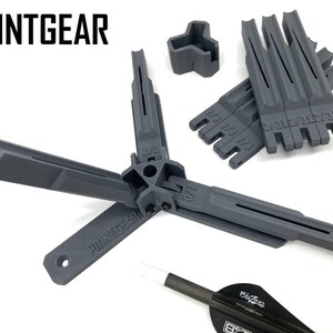 Könnte beinhalten: Eine Sammlung grauer 3D-gedruckter Werkzeuge und Zubehörteile, darunter eine mehrteilige Baugruppe mit dem Text "PRINTGEAR" und ein Dartpfeil. Die Werkzeuge haben verschiedene Schlitze und Maße, und der Dartpfeil hat einen schwarzen Schaft und eine weiße Spitze.