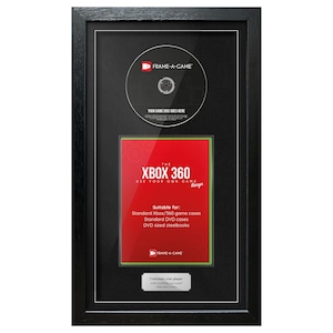 Op de afbeelding: Zwart omkaderde display met een Xbox 360 game case en disc. De rode game case insert heeft witte tekst "THE XBOX 360 USE YOUR OWN GAME". De disc staat boven de game case, en de lijst heeft een zwarte rand.