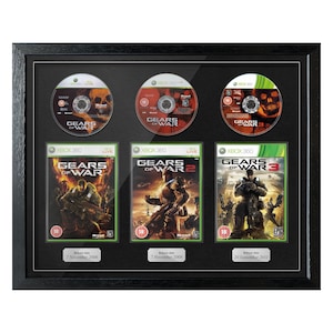 Puede incluir: Colección enmarcada de videojuegos Gears of War, con tres discos de juego y sus correspondientes cajas de juego de Xbox 360. El marco negro muestra los juegos con sus fechas de lanzamiento.