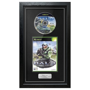 May include: Framed Xbox game, "Halo: Combat Evolved," with the game disc above the box art. The box art features a green-armored soldier. The frame is black, and a small plaque at the bottom reads "Release date 15 November 2001."