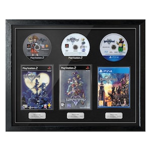 Puede incluir: Exhibición enmarcada de videojuegos Kingdom Hearts. Incluye discos y cajas de juegos de PlayStation 2 y PS4, con fechas de lanzamiento. El marco negro resalta los juegos.