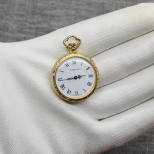 Peut inclure: Une montre de poche dor&eacute;e avec un cadran blanc et des chiffres romains noirs. Le cadran de la montre indique "Dianfus".