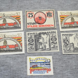 May include: A selection of vintage German stamps and labels. The stamps feature illustrations of buildings, cityscapes, and text in German. Some stamps have the text "50 Pfennige" and "Zwei Mark". The color palette includes red, orange, and black.