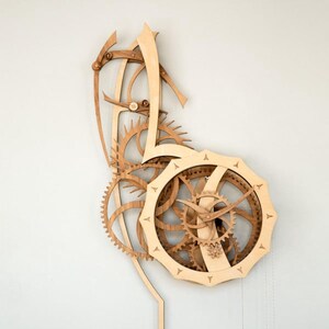 May include: A wooden wall clock with exposed gears and a unique design. The clock features a light-coloured wood frame and intricate gear mechanisms in shades of brown. The clock's hands are visible, and the overall aesthetic is a blend of art and functionality.