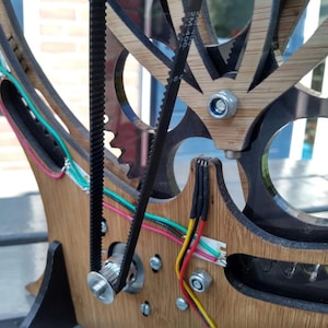 May include: Close-up of a wooden and metal machine with black belts and wires. The machine has a circular design with gears and a motor.