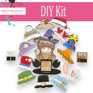 May include: DIY kit featuring a wooden Highland Cow with various hats and signs. The hats include a witch hat, a cowboy hat, a Santa hat, a birthday hat, a sombrero, a leprechaun hat, a graduation cap, a bunny ear headband, a flower hat, and a winter hat. The signs say "Welcome to our Herd", "I love fluffy cows", and "Home on the Farm".