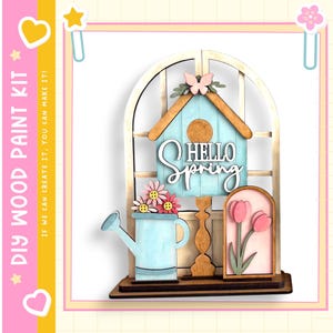 May include: DIY wood paint kit featuring a spring-themed design. The kit includes a light blue birdhouse with "Hello Spring" text, a watering can, and a framed tulip design. A butterfly and flowers add decorative touches.