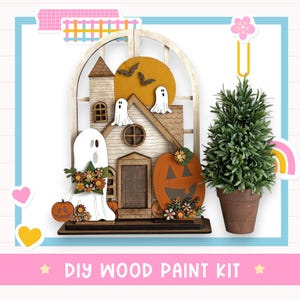 May include: A wooden Halloween-themed DIY paint kit featuring a house with a pumpkin, ghosts, and bats. The kit includes a small potted evergreen tree. The text "DIY WOOD PAINT KIT" is at the bottom of the image.