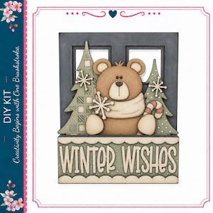 May include: A DIY kit featuring a wooden cutout of a brown bear wearing a scarf, positioned in front of a dark window frame with two green patterned pine trees and white snowflakes. A rectangular base displays the text WINTER WISHES.