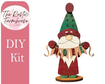 May include: A wooden gnome figurine DIY kit featuring a green hat with snowflake patterns, a red coat with heart and snowflake details, and a white beard. The gnome holds a banner with the letters N, O, E, L in red and green on tan flags.