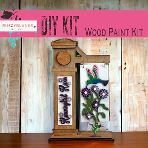 May include: DIY wood paint kit featuring a hummingbird and flowers. The kit includes a wooden sign with the words "Hummingbird Haven" and a separate wooden panel with a hummingbird and flowers. The kit is ready to be painted.