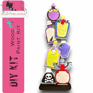 May include: A wooden DIY paint kit featuring a stack of six potion bottles with labels that read "Black Cat Hisses", "Bat Wings Tonic", "Rat Tails", "Arsenic Poison", "Tarantula Venom", and "Dragon Blood".