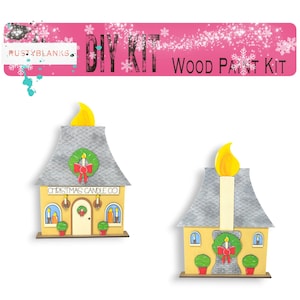 May include: DIY wood paint kit featuring two Christmas candle shop buildings. The buildings are yellow with gray roofs and white trim. Each building has a wreath on the front and a lit candle on the roof. The text "Christmas Candle Co." is on the front of one building.