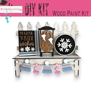 May include: DIY wood paint kit featuring a winter scene with a white picket fence, a sign that says "Warm Winter Wishes", a wooden sled, a snowflake, and a garland of hats and mittens.