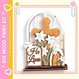 May include: DIY wood paint kit featuring a wooden cross, lilies, and the text "He Lives." The kit includes a wooden window frame, a dove, and a tomb. The design is in shades of brown, white, and green.