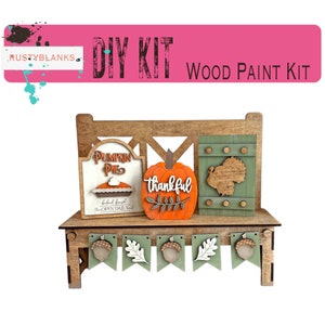 May include: DIY wood paint kit featuring a wooden bench with a pumpkin pie sign, a pumpkin with the word "thankful" on it, and a turkey sign. The bench has a green and brown banner with acorns and leaves hanging from it.