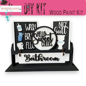 May include: A black and white DIY wood paint kit with bathroom-themed decor. The kit includes signs with text like "Wash," "Nice Butt," and "Bathroom." The kit also includes a sign that says "Hello Sweet Cheeks."