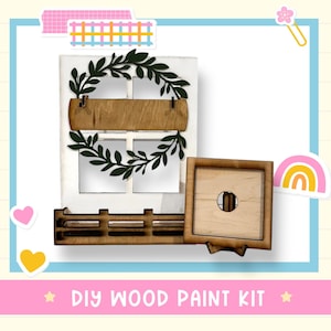 May include: A DIY wood paint kit featuring a white window frame with a dark green leaf wreath, a horizontal wooden sign, and a window box. A separate square wooden frame with a circular center cutout is included. The text DIY WOOD PAINT KIT is visible.
