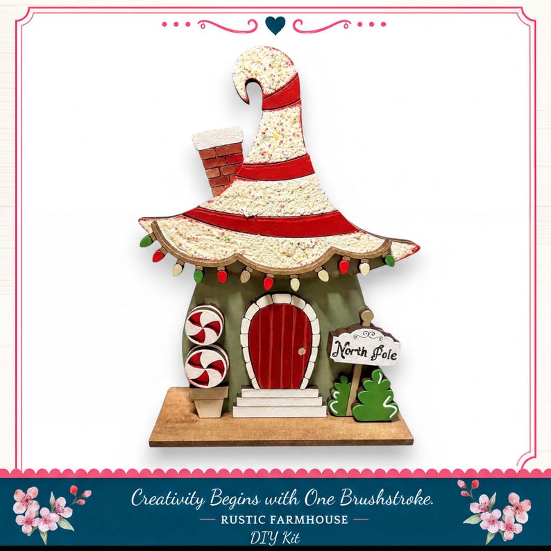 A whimsical, handcrafted Christmas ornament resembling a small house with a pointed roof, red door, and a sign that reads "North Pole". The ornament is decorated with candy canes and other festive elements, creating a charming holiday scene.