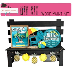 May include: DIY wood paint kit featuring a black wooden bench with a summer theme. The kit includes a sign that says "Summer Vibes" with palm trees and the text "Beach 1/2 mi", a beach chair, an umbrella, a beach ball, and a round sign that says "Hello Summer". The bench also has a garland of pineapples and suns.