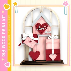 May include: DIY wood paint kit featuring a pink house with a heart-shaped door and mailbox. Includes a red heart with the word "love", a mailbox with an envelope, and stacked gift boxes. The kit includes the text "If we can create it, you can make it!"