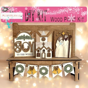 May include: DIY wood paint kit featuring a Christmas scene with a church, a nativity scene, and a "Joy to the World" sign. The kit also includes a banner with wreaths and bells.